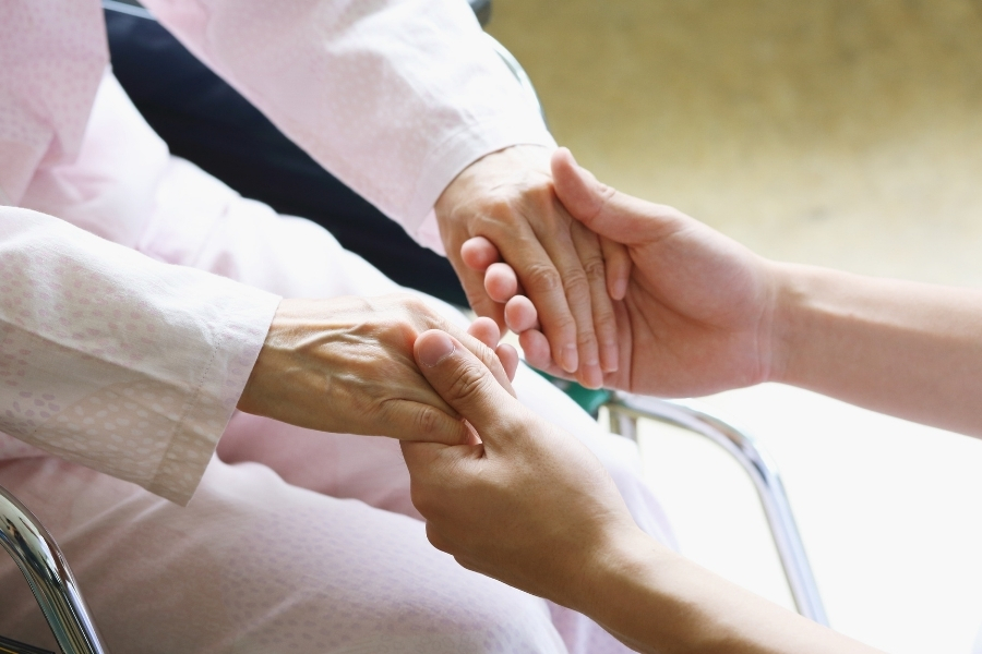 Pflegekraft hält Hände von pflegebedürftiger Seniorin